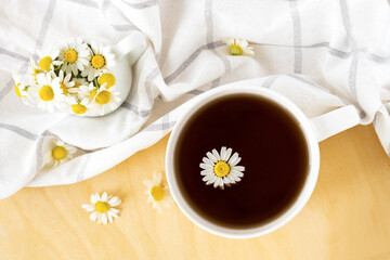 Chamomile tea with kitchen towel and chamomile in white ceramic cup on the wooden table. Herbal tea. Top view. Flat lay