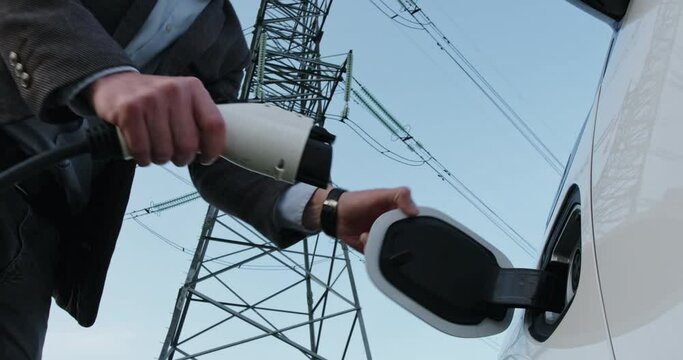A man connects his electric car to charging from a centralized electrical network. The concept of using an electric car as an akumulator of an electrical network.