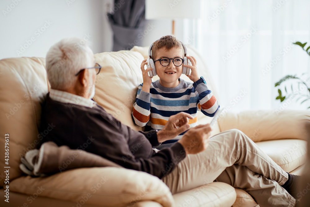 Wall mural happy kid listening music over headphones while spending time with grandfather at home.