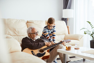 Grandfather teaching his grandson to play acoustic guitar while spending time together at home.