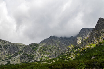 Fototapeta premium Landscape with high stone sharp rocky peaks under cloudy sky in National Park High Tatras Mountains, Slovakia. Tourist destination for hiking and tourism