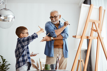 Happy grandfather and grandson having fun while painting together at home.