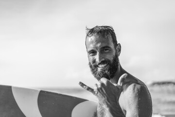 Surfer happy with surf surfing smiling doing hawaiian shaka hand sign for fun during surf session...