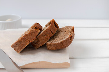 Slices of fresh rye bread on wooden board on white table with space for text