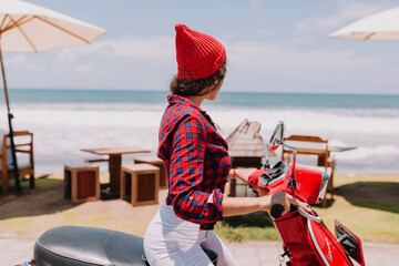 Close up portrait of young woman from back wearing cap and stretched shirt looking at the ocean...