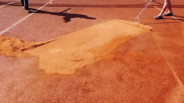 Maintenance of a clay tennis court. Laying a new layer of brick dust, chamotte, and leveling the court surface by hand. Preparing for the new playing season, training and competition.