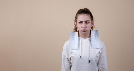 Sad, beautiful young brunette girl with the mask removed on her ears. She is unhappy. Medicine. Coronavirus. Vaccine for Covid. Pandemic. Disease. Place for an inscription. Advertising. Protest.