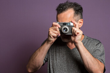 Fototapeta premium Portrait of a professional photographer isolated on a purple background taking a picture with a vintage camera.