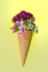 Still life with an ice cream cone, on a yellow background. In the bag there are many colorful flowers, so-called mustaches, which are in the waffle instead of the ice cream