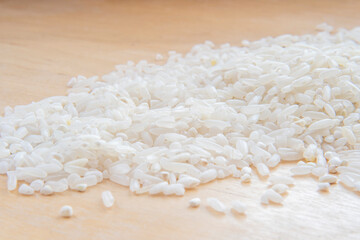 Raw rice grains on a wooden surface. Light background blurry in soft focus at high magnification.