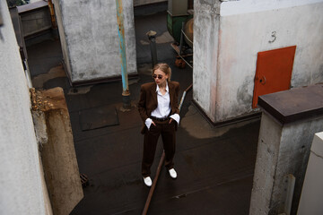 Fototapeta na wymiar high angle view of stylish blonde woman looking away while posing with hands in pockets on rooftop