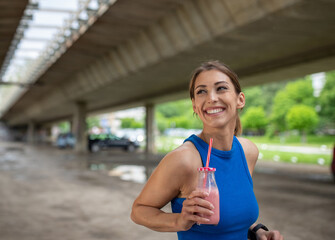 Smiling female athlete standing in parking lot holding milkshake