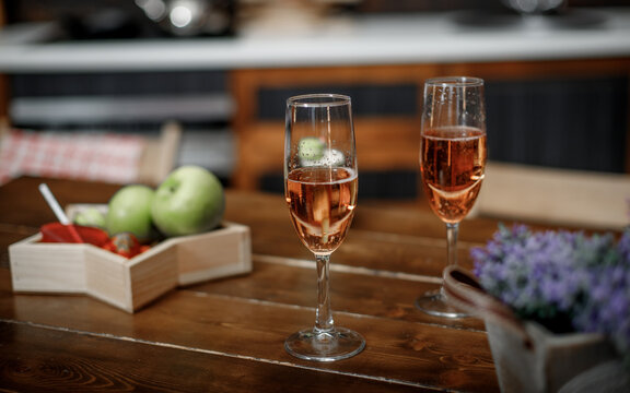 Champagne in glasses and a bowl of fruit on a wooden table top in a cafe.