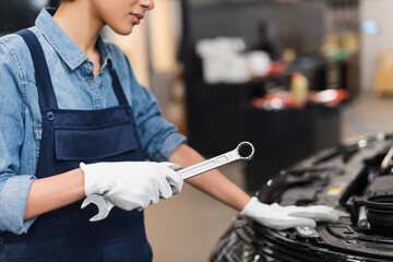 partial view of young african american mechanic holding wrench near car hood in garage