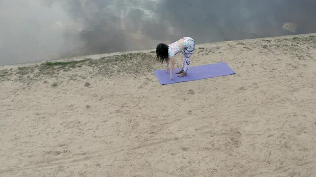 A woman practicing yoga in the nature on the beach near the lake in the evening at sunset in loneliness