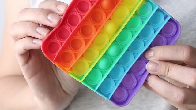 The girl presses her fingers on a square-shaped silicone toy pop it. Close-up simple dimple game. Anti-stress thing.