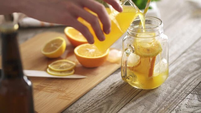Prepares summer soft drinks, cold sweet and sour orange juice is poured into a glass with sliced ​​fresh lemons and oranges. Refreshing summer drink. Traditional lemonade with ice cubes.