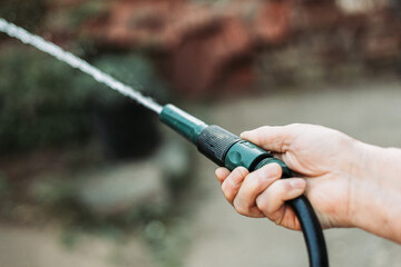 Female hand holding gardening hose, watering garden