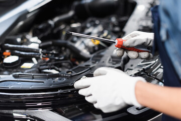 close up view of female mechanic hands in gloves repairing car motor with screwdriver in garage