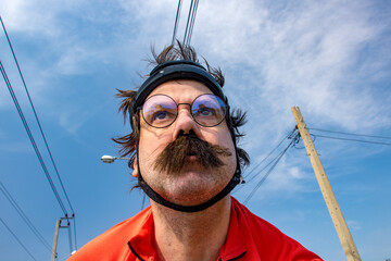 Portrait of cyclist in retro helmet riding a bicycle in summer landscape, blue sky background. The adult biker with mustache ride on road bike under cables.