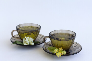 cup of tea. two dark glass cups with herbal hot linden tea and jasmine tea with bloom flowers isolated on white background. healthy drink in black mugs with green leaves on the table. copy space.