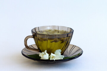 cup of tea. dark glass cup with herbal hot jasmine tea with bloom flowers of jasmine isolated on white background. healthy drink in black mug with green leaves on the table. copy space.