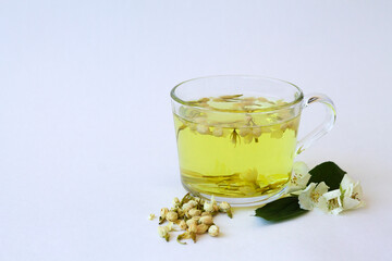 herbal tea with flowers. glass cup with herbal hot jasmine tea with bloom flowers of jasmine isolated on white background. healthy drink in mug with green leaves on the table. copy space