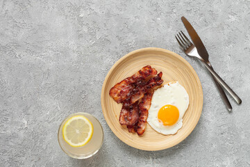 Keto breakfast with fried eggs, bacon and lemonade on grey background