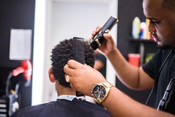 peluquero cortando el pelo a joven en barberia latina.con maquina de cortar el pelo cuidadosamente frente al espejo.con reloj y anillo .