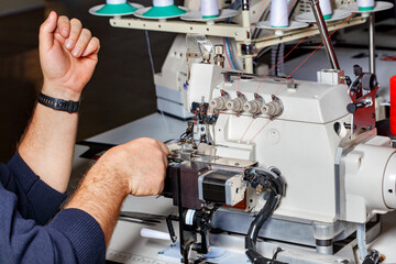 The master adjusts the mechanisms of a modern electric overlock.