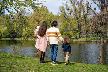 Young family staying in a park and holding hands, turned backs into the camera and engoying the...