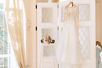 Accessories for the morning of the bride, in a light studio. Wedding dress on a hanger, shoes, mirror, boudoir.
