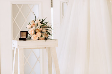 Wedding gold rings in a box next to a bouquet, on a light background.