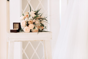 Wedding gold rings in a box next to a bouquet, on a light background.