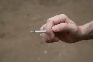 The man's hand holds a smoking cigarette. Smoking on the street.