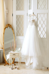 Accessories for the morning of the bride, in a light studio. Wedding dress on a hanger, shoes, mirror, boudoir.