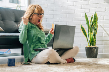 woman with laptop computer at home sitting comfortably on the floor celebrating success
