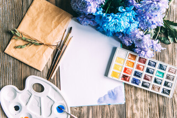 Palette of watercolor paints, brushes and paper for a water color on wooden background, close up. Flat lay, spring background with copy space