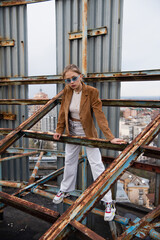 full length of young and pretty woman in stylish outfit and sunglasses standing on weathered construction of rooftop