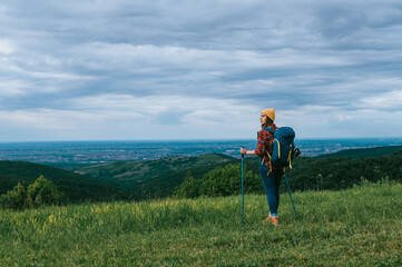 Naklejka na ściany i meble A young hiker woman using trekking poles and wearing backpack