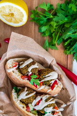 Top view on a fresh falafel balls inside of two halves of pita bread sandwich with chopped salad, red hot peppers, lemon, a drizzle of tahini sauce. chickpea falafel in a fluffy pita on a wooden board