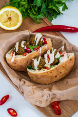 Authentic fresh falafel balls inside of two halves of pita bread sandwich with chopped salad, red hot peppers, lemon and a drizzle of tahini sauce. chickpea falafels in a fluffy pita on a wooden board