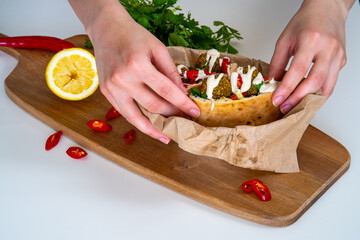 Woman hands hold an authentic half of pita bread sandwich with fresh falafel balls inside and chopped salad and drizzle of tahini sauce on top, close-up of chickpea falafel in a fluffy pita