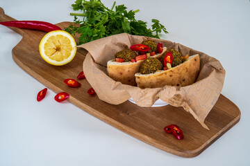 Authentic fresh falafel balls inside of two halves of pita bread sandwich with chopped salad, red hot peppers, lemon, a drizzle of tahini sauce. chickpea falafel in a fluffy pita on a wooden board