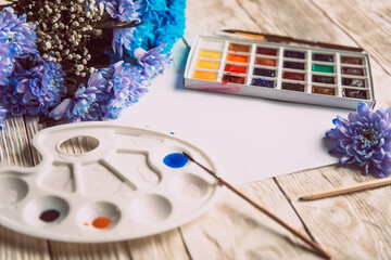 Palette of watercolor paints, brushes and paper for a water color on wooden background, close up. Flat lay, spring background with copy space