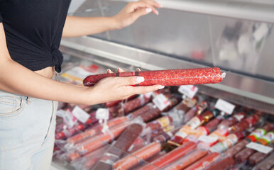 Caucasian woman buying sausage in supermarket.