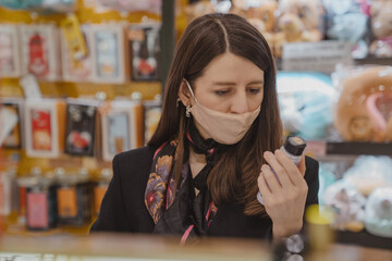 Young woman wearing face mask shopping choosing beauty products in the store. New normal, protection, safety concept. Close up