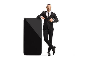 Full length portrait of a young professional man standing next to a big smartphone and pointing