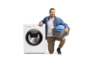 Smiling young man kneeling next to a washing machine and holding a loundry basket