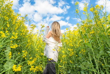 Fototapeta premium Young woman stands in a rapeseed field and looks into the blue sky
